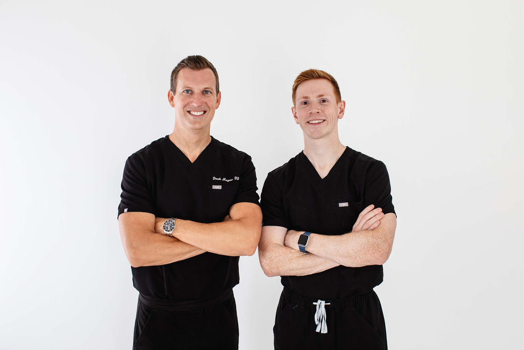 Two dentists standing side by side in black scrubs, smiling