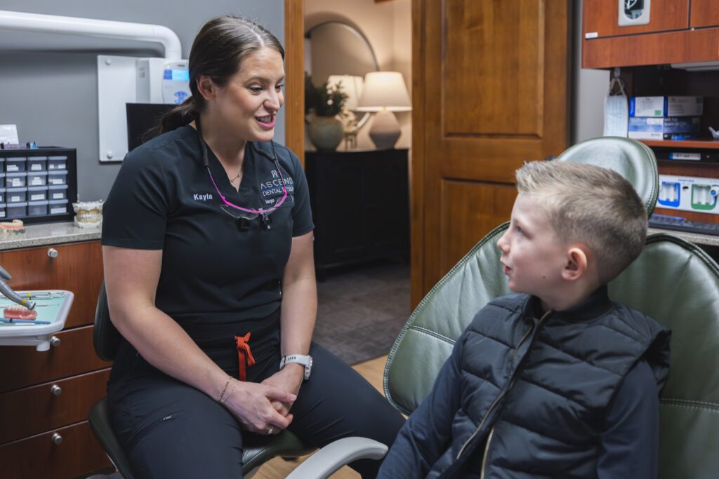 Dental hygienist speaking with young patient in treatment room